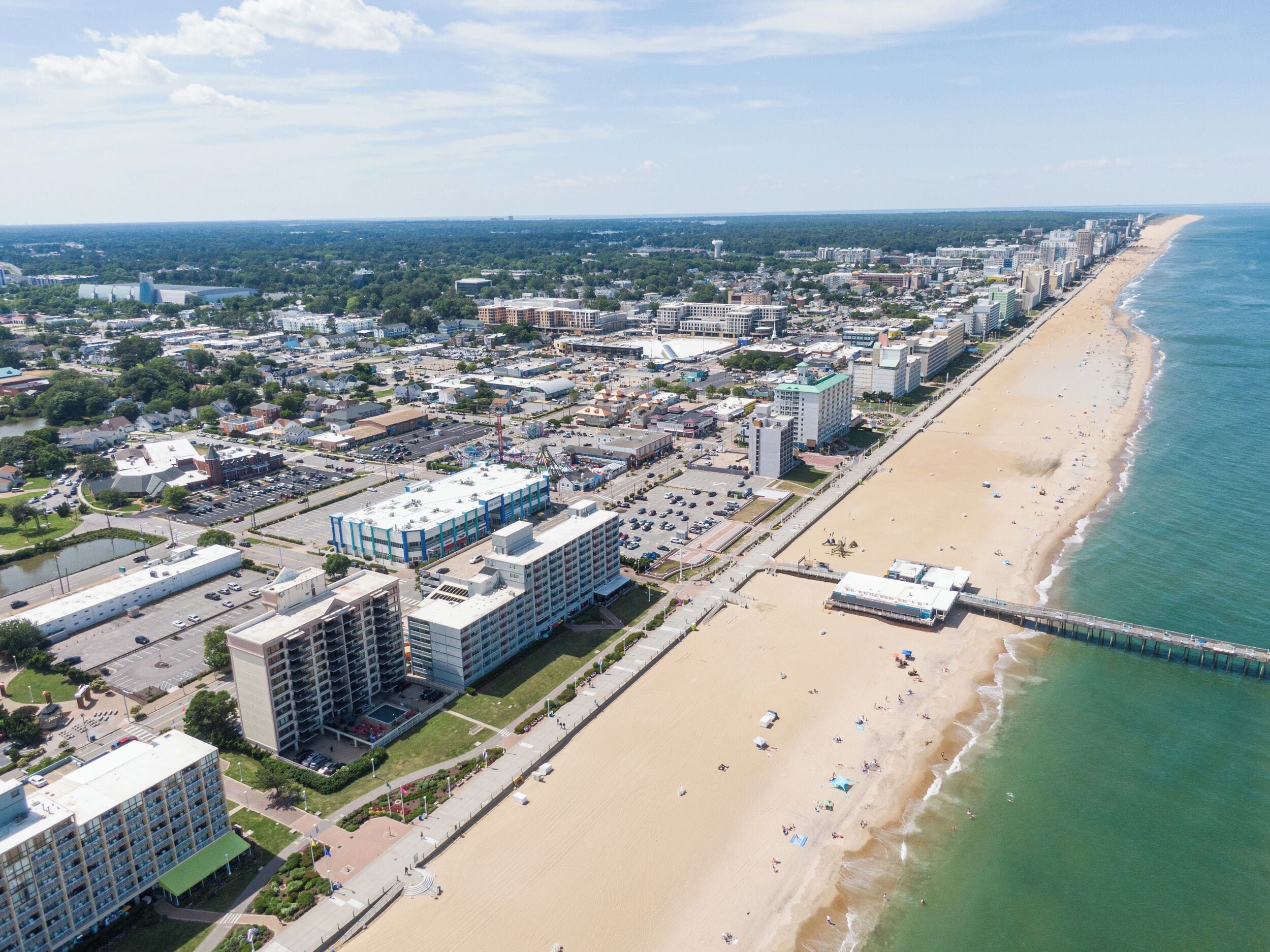 An aerial view of a coastal city with a long beach, a pier, and various buildings including hotels and commercial areas.