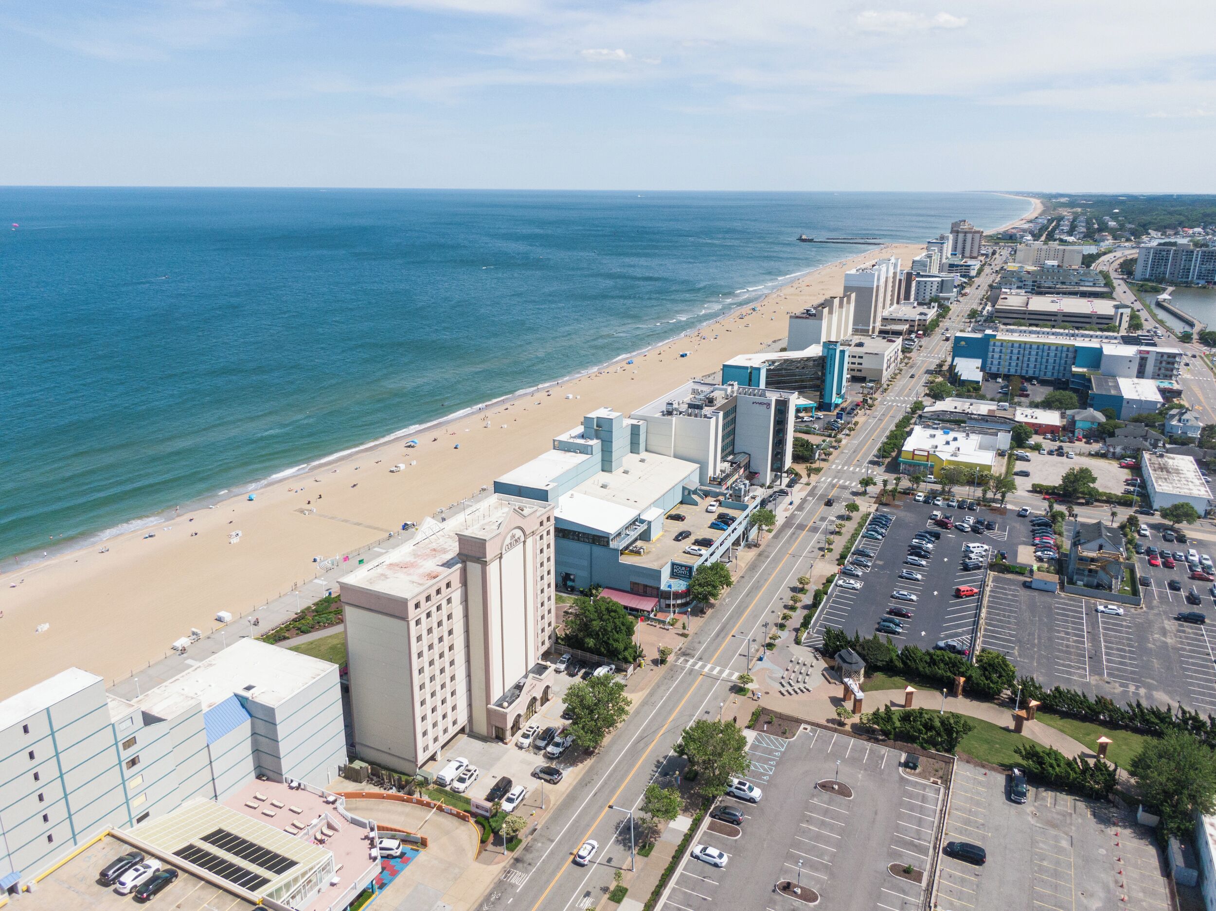 A coastal cityscape with a beachfront hotel, parking lots, and a clear view of the ocean.