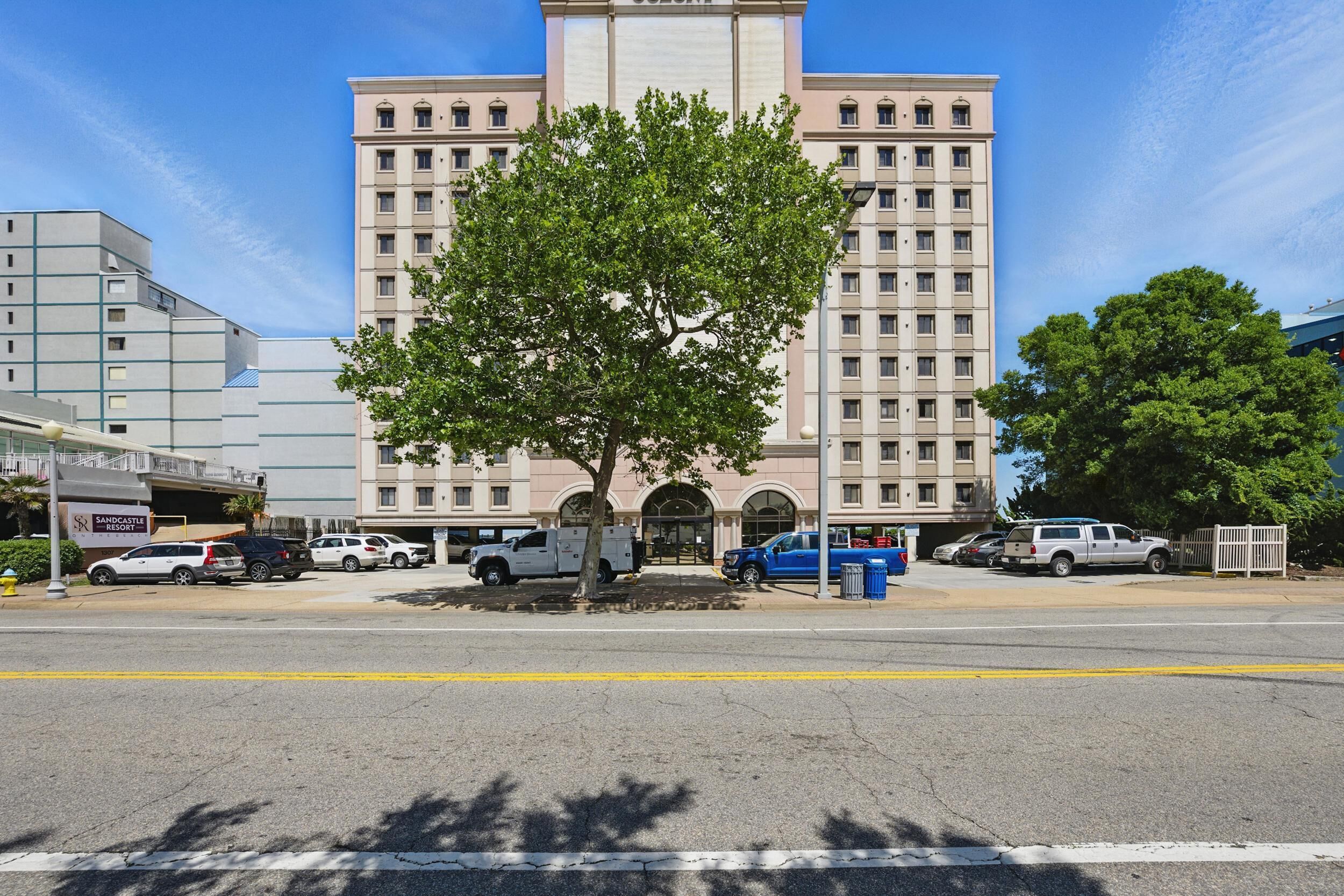 A multi-story building with a central entrance, surrounded by parked vehicles and trees.