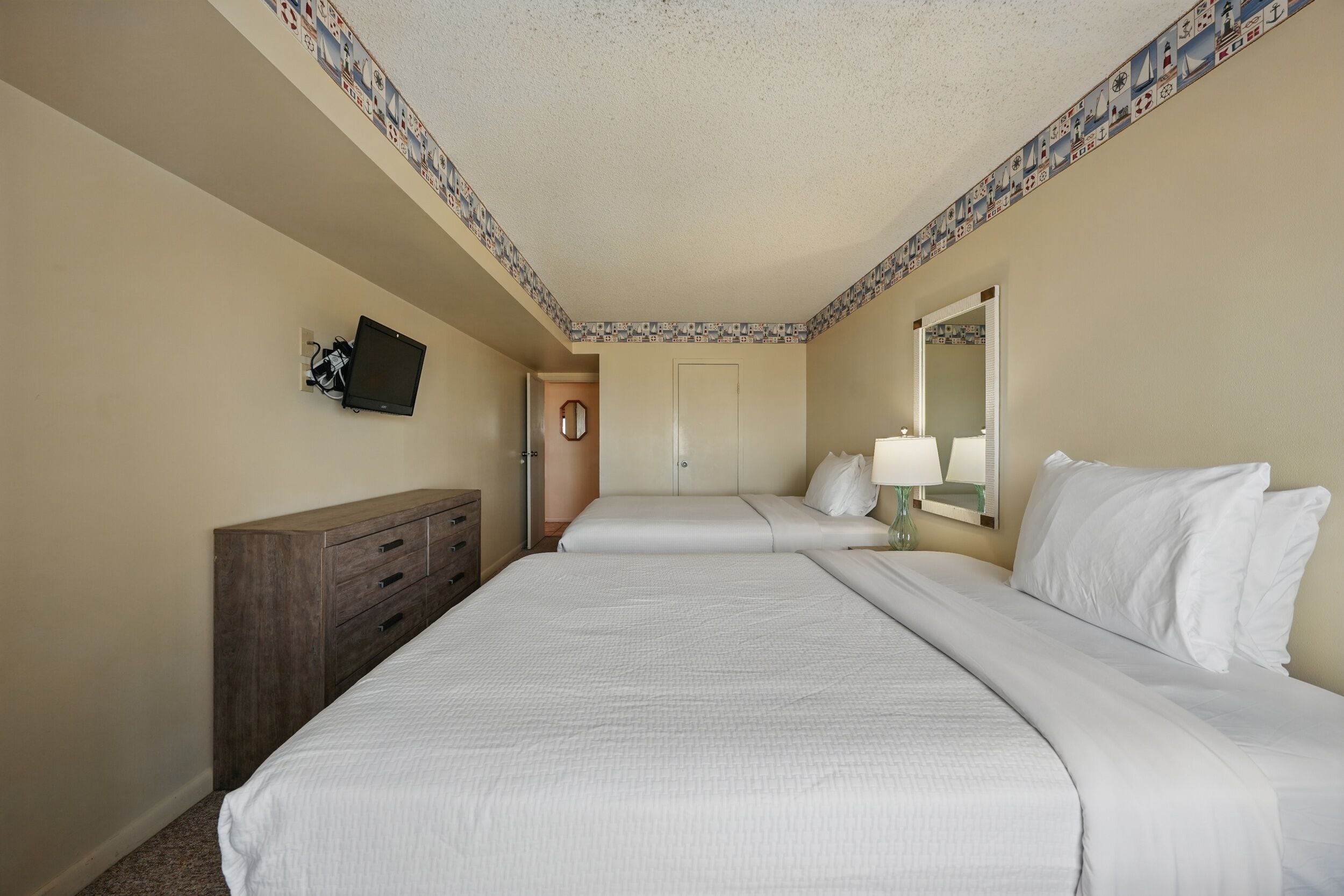 Une chambre d’hôtel avec deux lits, une commode, un téléviseur à écran plat, un miroir et une porte donnant sur une autre pièce.