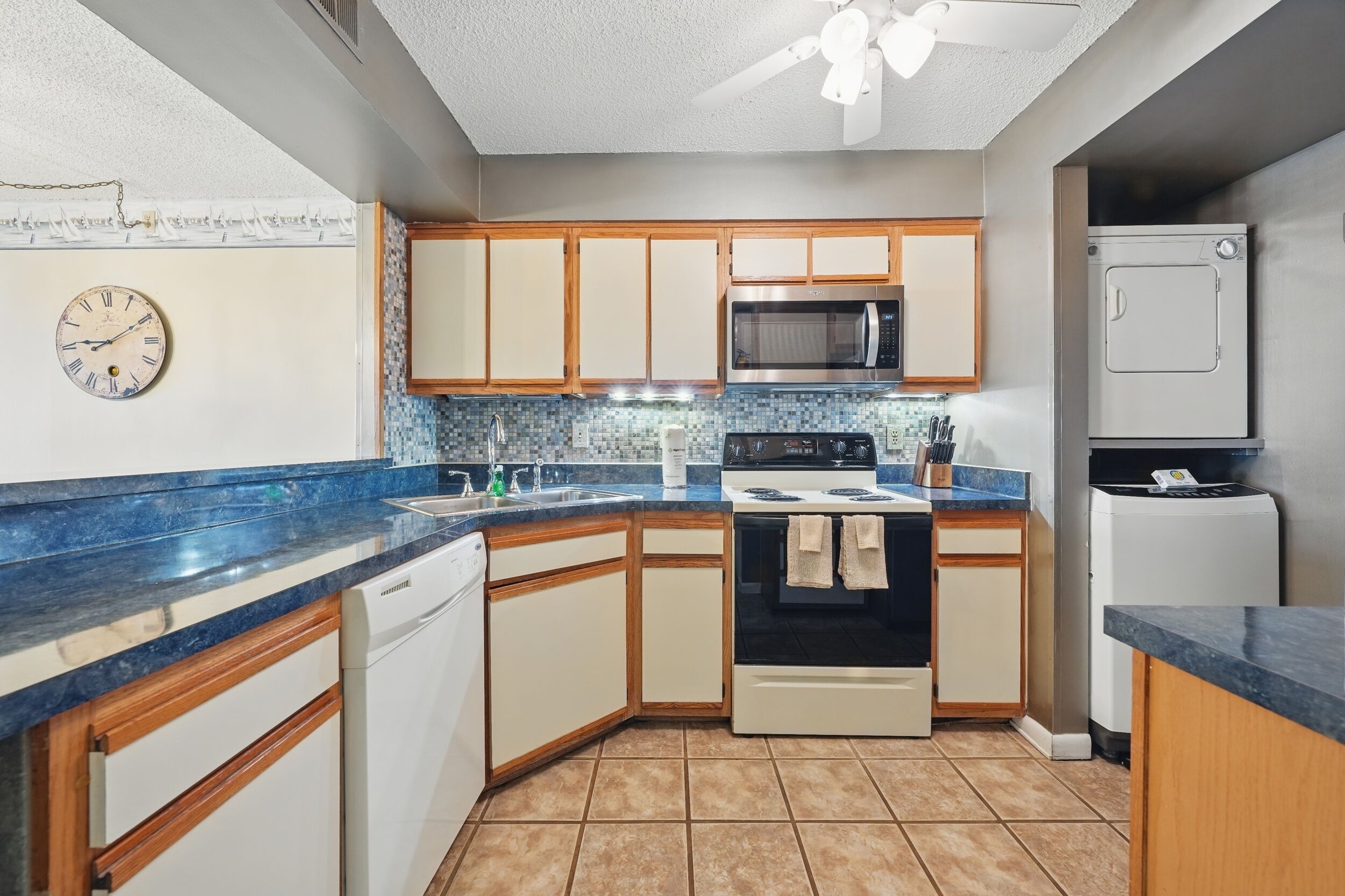 A kitchen with wooden cabinets, a microwave, an oven, a dishwasher, and a clock on the wall.