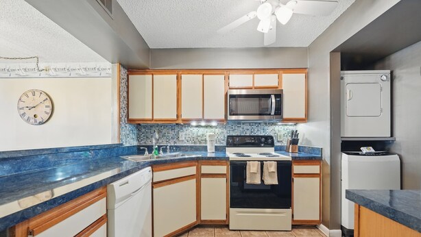 A kitchen with wooden cabinets, a microwave, an oven, a dishwasher, and a clock on the wall. - The Colony at Virginia Beach (Virginia Beach)