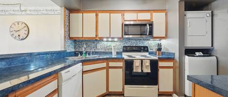A kitchen with wooden cabinets, a microwave, an oven, a dishwasher, and a clock on the wall.