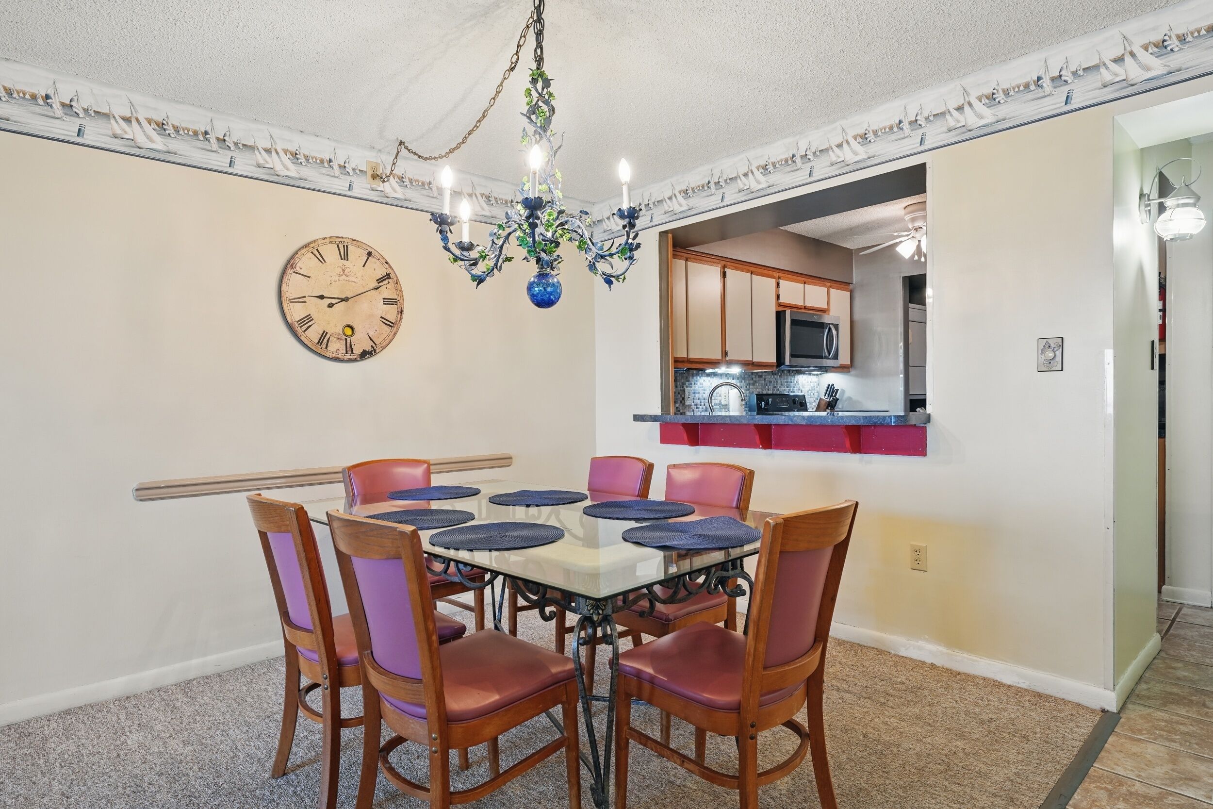 A dining room with a round table, six chairs, a wall clock, and a chandelier.