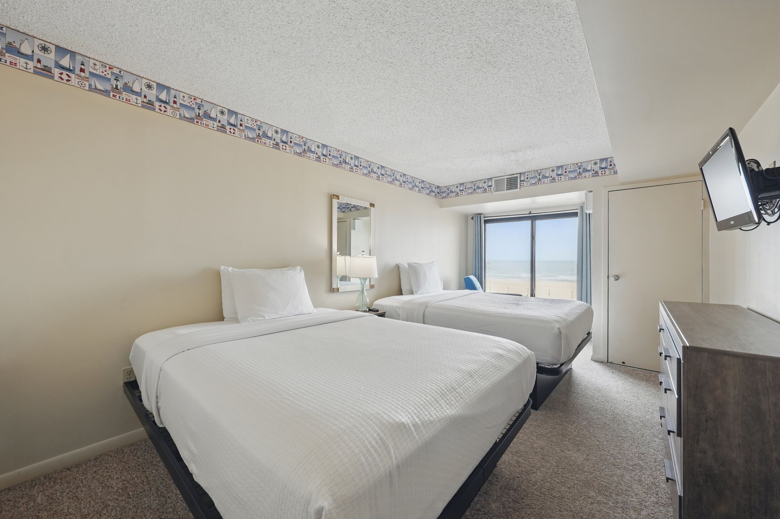 A hotel room with two beds, a large window, a television, and a dresser.