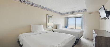 A hotel room with two beds, a large window, a television, and a dresser.