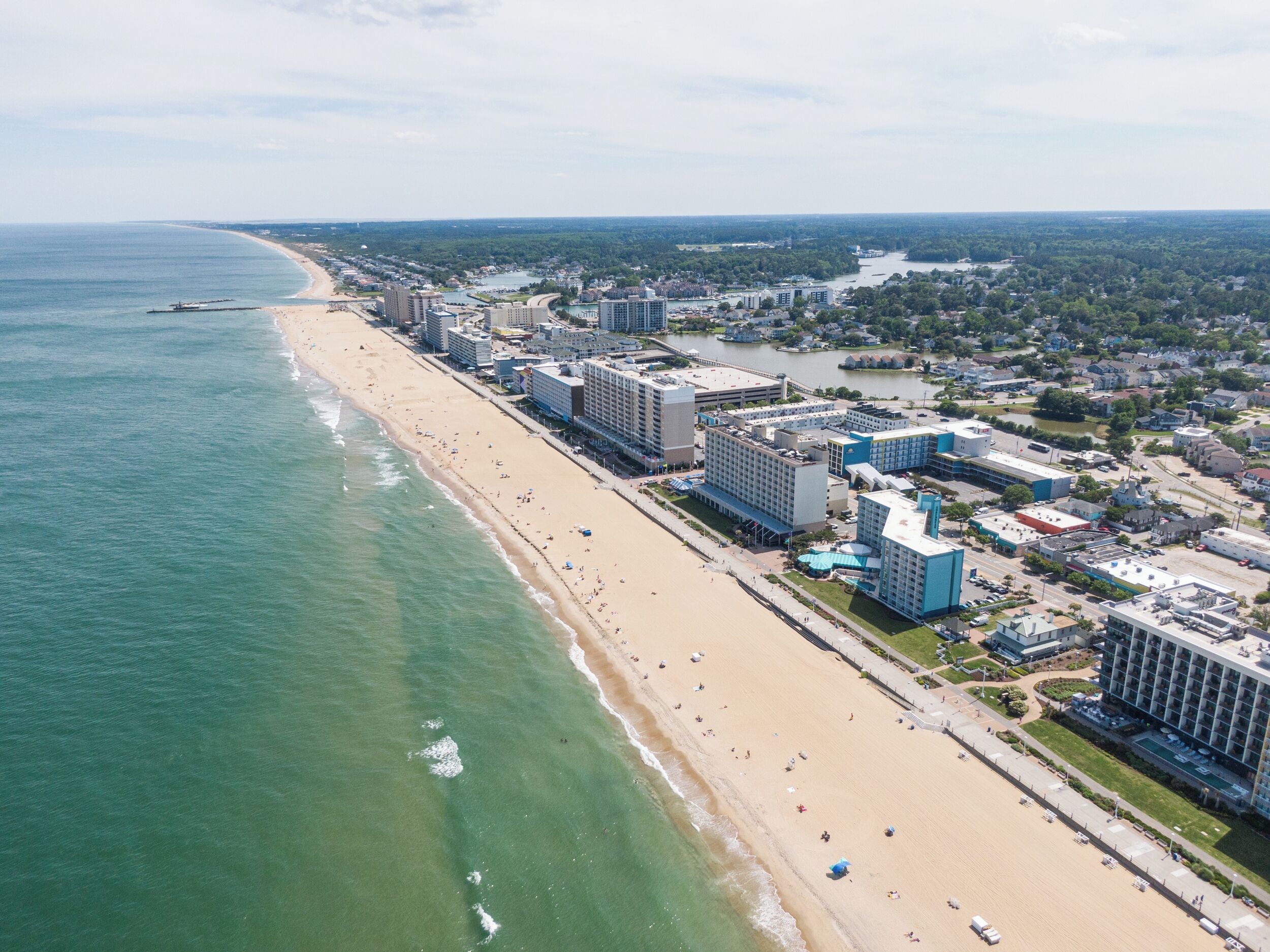 An aerial view of a coastal city with a long sandy beach, high-rise hotels, and a river running parallel to the shore.
