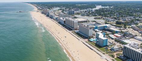 An aerial view of a coastal city with a long sandy beach, high-rise hotels, and a river running parallel to the shore.