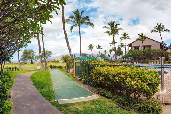 A well-maintained outdoor area with a walking path, a shuffleboard court, and a pool area with lounge chairs.
