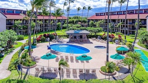 Un hotel con piscina central, sillas de descanso y palmeras.