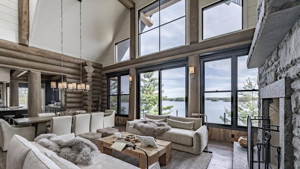 A spacious living room with a fireplace, large windows offering lake views, and a cozy seating area. - 9 bed 9 bath log home on Lake Muskoka (Bracebridge)