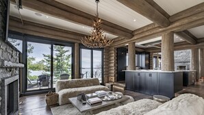 A spacious living area with a stone fireplace, a large chandelier, and a view of the outdoors. - 9 bed 9 bath log home on Lake Muskoka (Bracebridge)