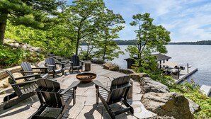 An outdoor patio with Adirondack chairs, a fire pit, and a view of a lake. - 9 bed 9 bath log home on Lake Muskoka (Bracebridge)