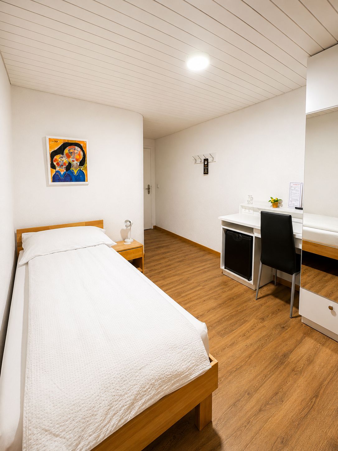 A room with a bed, a desk, a chair, and a small kitchenette.