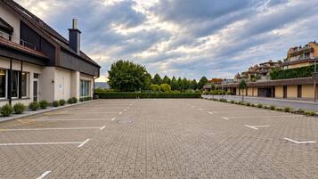 A paved parking area with marked parking spaces, surrounded by modern buildings with flat roofs and a clear sky above.