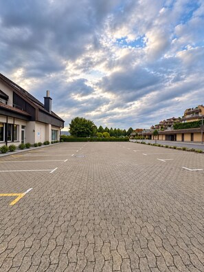 Un área de estacionamiento pavimentada con espacios delimitados, rodeada de edificios modernos con techos planos y un cielo despejado.