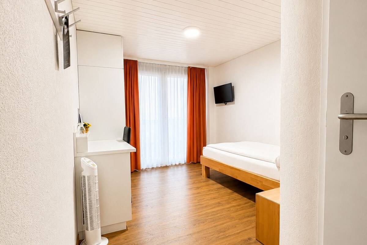 Une chambre d’hôtel avec un lit, un bureau, une chaise, une télévision et une fenêtre avec des rideaux.