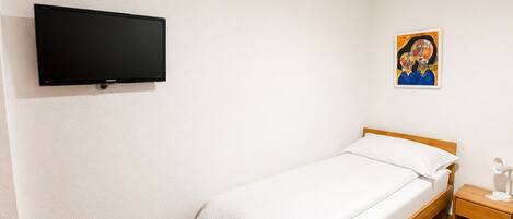 Een slaapkamer met een bed, een tv aan de muur, een nachtkastje en een schilderij.