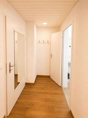 Un couloir étroit doté d’un plancher en bois, de murs blancs et d’un plafond pourvu d’un éclairage encastré.