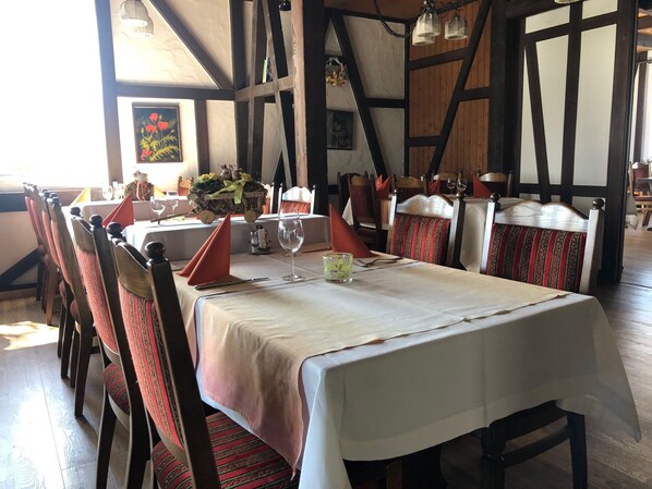 Un coin repas avec une longue table dressée pour six personnes, des chaises en bois avec des coussins à rayures rouges et vertes, et une nappe blanche.