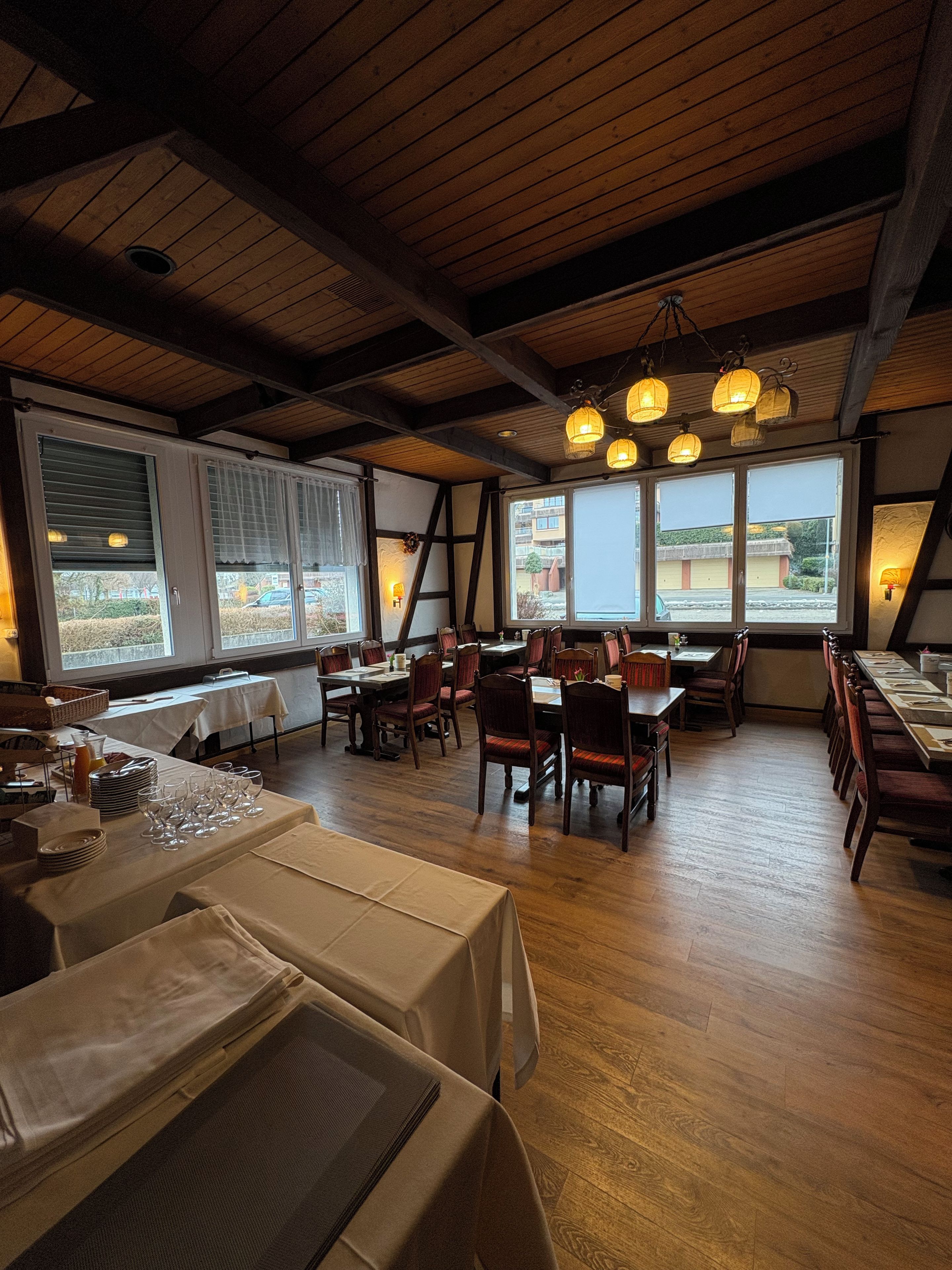 Een restaurant met houten balken, gedekte tafels en grote ramen met uitzicht.