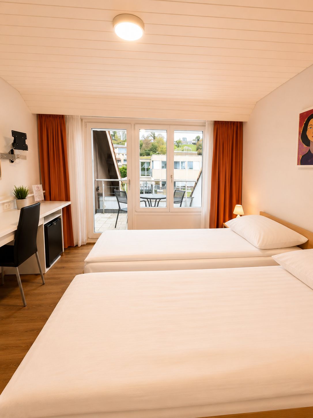 Ein Hotelzimmer mit zwei Betten, einem Schreibtisch, einem Stuhl und Blick ins Freie.