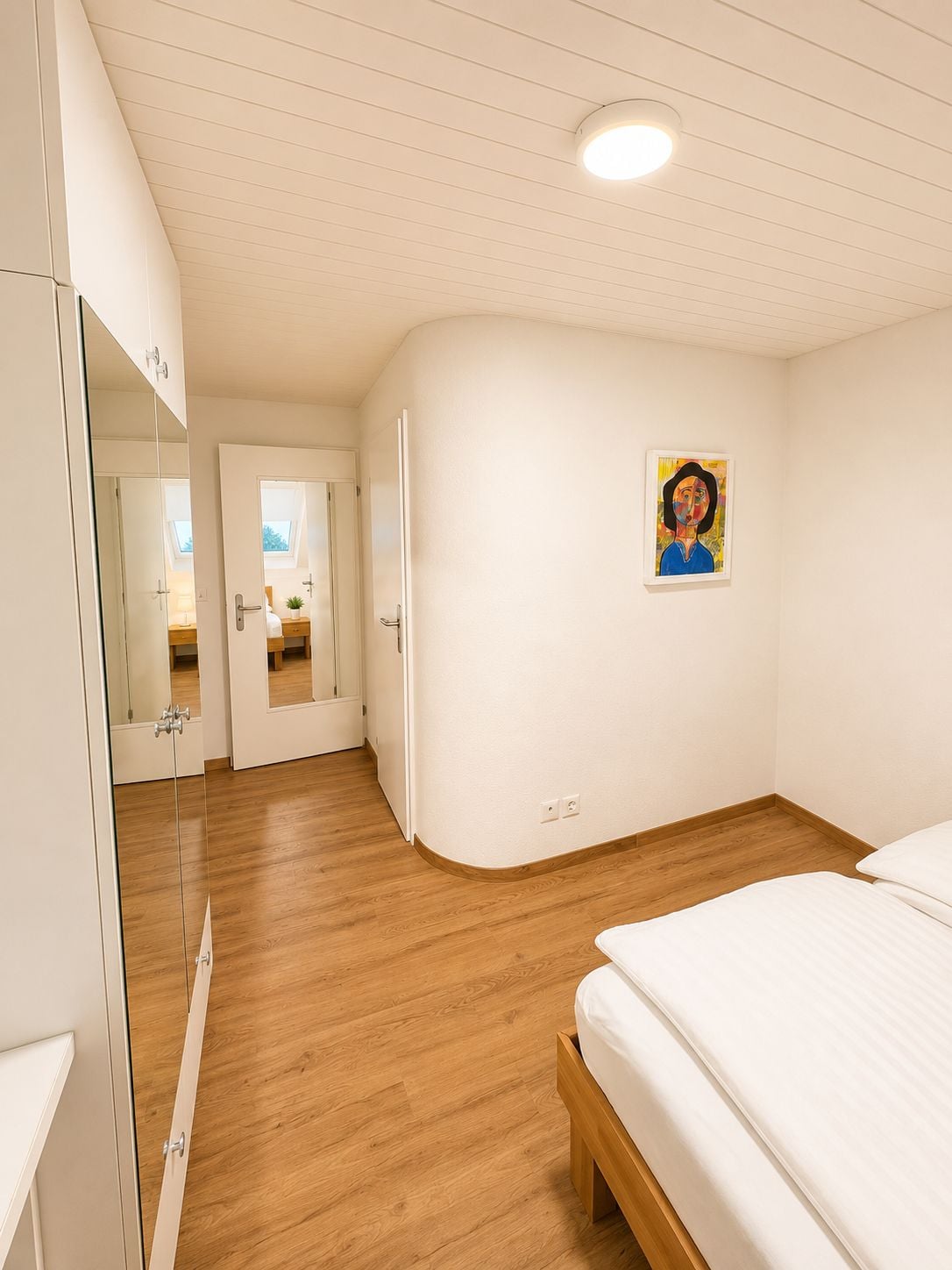 Un dormitorio con piso de madera, una cama, un armario y un cuadro en la pared.