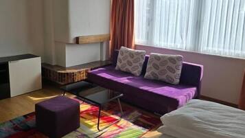 A room with a bed, a sofa, a small table, and a colorful rug.