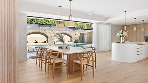 Eine moderne Küche mit Kochinsel, ein Essbereich mit Blick auf den Pool und ein geräumiger Wohnbereich mit großem Fenster, das auf ein Ziegelbogenwerk blickt.