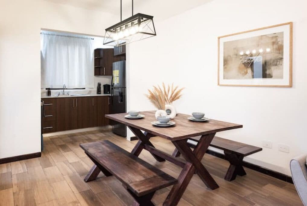 A modern dining area with a wooden table, benches, and a pendant light.