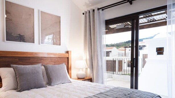 Un dormitorio con una cama grande, un cabecero de madera, una mesita de noche con una lámpara y vistas al exterior a través de una puerta corrediza de vidrio.