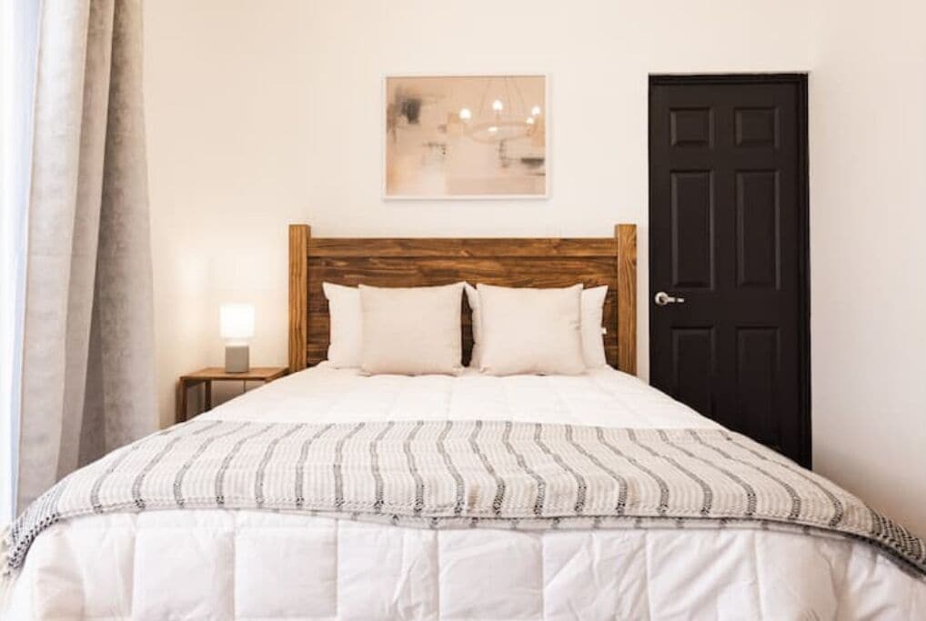 A neatly made bed with a striped blanket, a wooden headboard, a bedside lamp, and a framed picture on the wall.