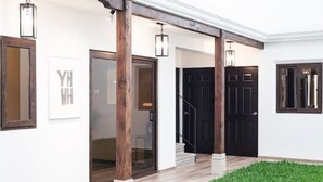 Una entrada de casa moderna con porche cubierto, una puerta negra y un pequeño jardín.
