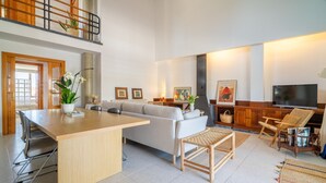 A spacious living area with a large sofa, a wooden coffee table, and a TV. There is a dining table with chairs and a balcony with a railing. - Rostoll Espai de Calma (Muro)