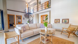 A spacious living area with a high ceiling, a spiral staircase, a sofa, a coffee table, and a wicker chair. - Rostoll Espai de Calma (Muro)