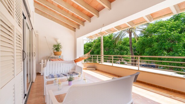 A balcony with a white wicker chair, a small table with a plant, and a view of lush greenery. - Rostoll Espai de Calma (Muro)
