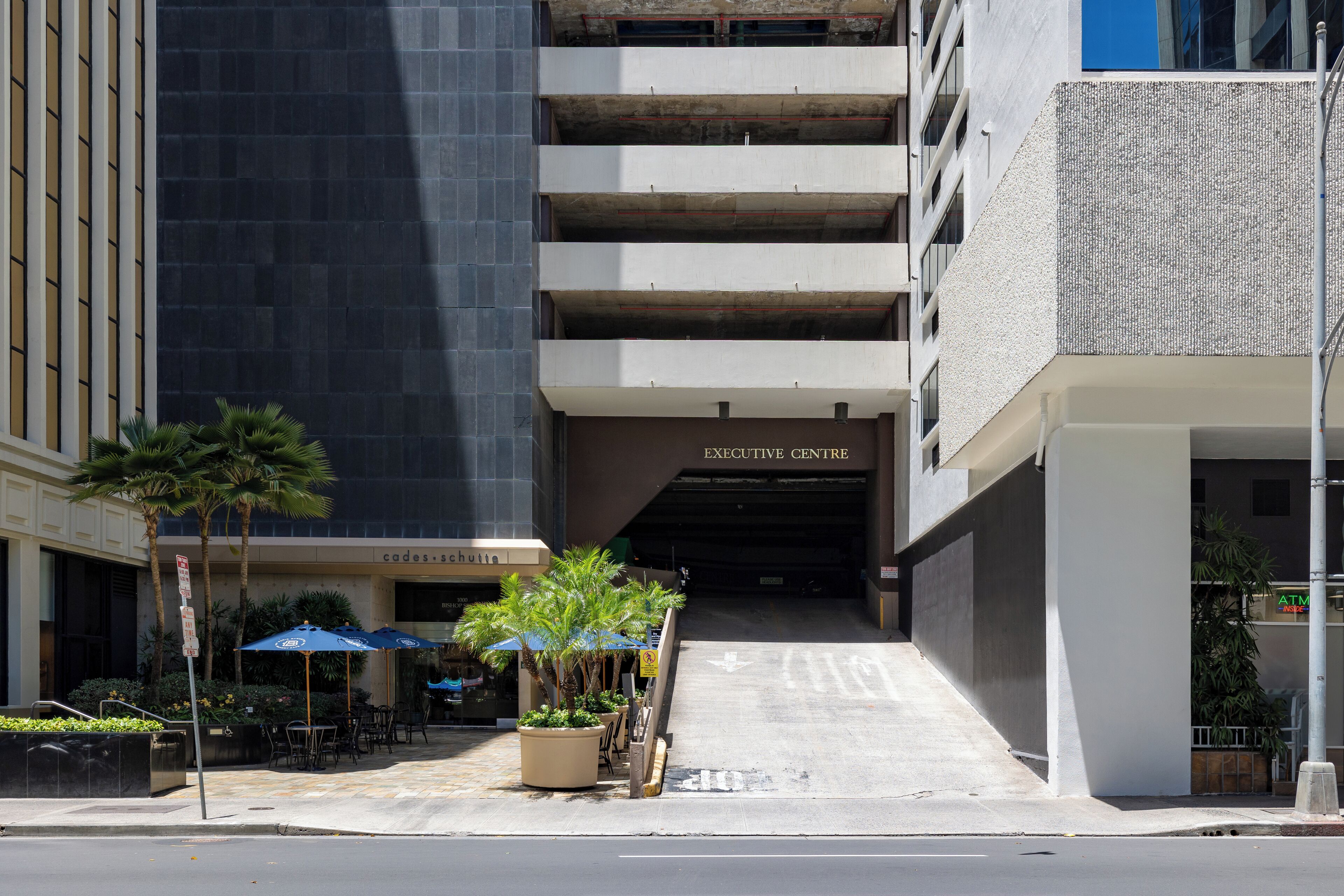 A building with an "EXECUTIVE CENTRE" sign, outdoor seating with umbrellas, and a staircase leading to the entrance.