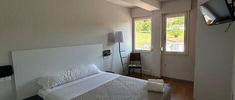 A bedroom with a bed, a nightstand, a chair, a TV, and a window.