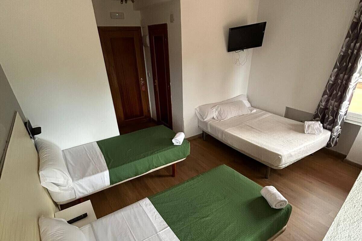 A hotel room with two single beds, a television, and a wooden floor.