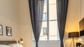 Une chambre à coucher bien rangée, avec un lit, une lampe de chevet, un bureau avec une lampe et une fenêtre avec des rideaux.