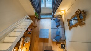 Un salon aux hauts plafonds comprenant un escalier, un ensemble de canapés, une table basse et un cadre photo fixé au mur.