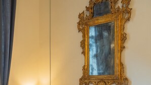 Une pièce avec un canapé bleu clair, un miroir encadré d’or et une lampe sur une table de chevet.