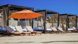 A beachside lounge area with sun loungers and an orange umbrella, surrounded by stone walls and wooden structures. - Cabo San Lucas Luxury Executive Suite with Ocean View - sleeps up to 6.  (Cabo San Lucas)