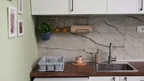 A kitchen with a marble backsplash, a wooden countertop, a sink, and hanging items like mugs and a plant.