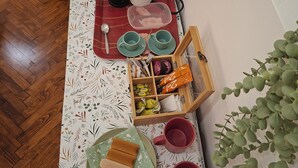 A dining table with a floral tablecloth, a tea kettle, cups, a tray with food, and a plant.