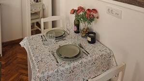 A dining table set with plates, cutlery, and a vase of flowers, with a painting of a forest scene on the wall behind.