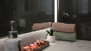 A bathroom with a marble countertop, a plant, towels, and a shower area.