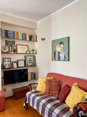 A living room with a red sofa, a television, and a bookshelf filled with books and framed items. - Elegant and spacious apartment by the sea! (Póvoa de Varzim)