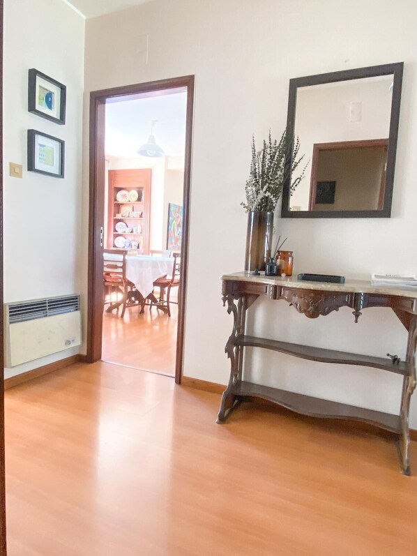 A room with a wooden floor, a table with chairs, a vase with flowers, a mirror, and framed pictures on the wall. - Elegant and spacious apartment by the sea! (Póvoa de Varzim)