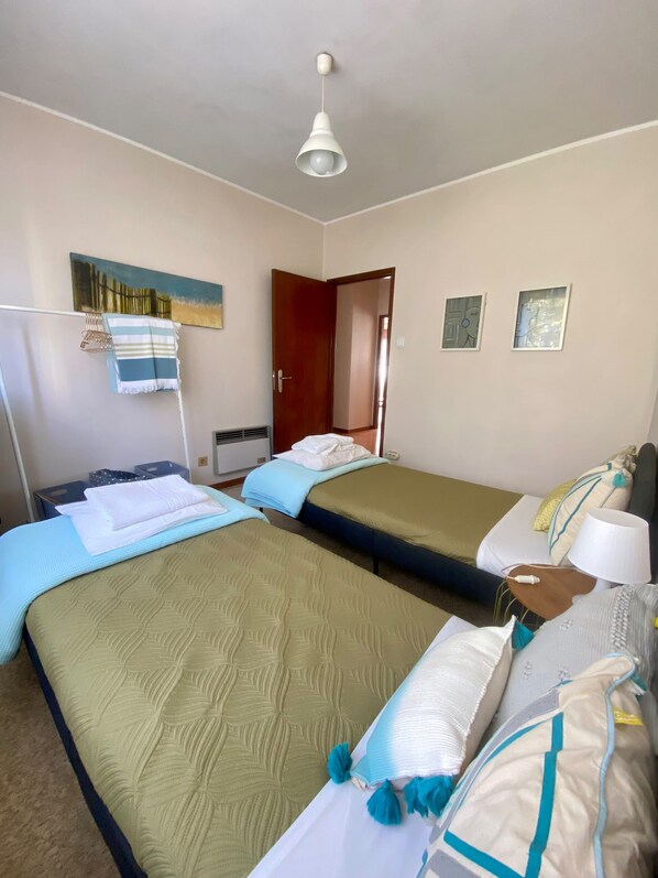 A hotel room with two beds, a heater, a painting, and a door leading to another room. - Elegant and spacious apartment by the sea! (Póvoa de Varzim)